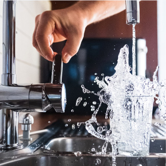 services-water Hand on a faucet pours clean, clear water into a water glass in the sink.